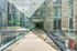 Glass-enclosed elevated walkway with stone floors, modern metal fixtures, and courtyard views in an urban residential complex.
