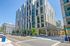 Exterior view of Apartments at City Center showing modern glass and stone architecture with retail stores on the ground level and a sunny city street.