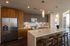 Contemporary apartment kitchen with stainless steel appliances, wood cabinetry, a large island with seating, and modern pendant lighting.