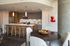 Modern apartment kitchen with wooden cabinets, a large island with bar stools, pendant lighting, and an adjacent dining area with contemporary decor.