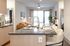 Open kitchen island with bar seating facing a bright living area with large windows, a tan sofa, and contemporary decor.