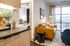 View from the kitchen showing a warm-toned leather sofa in the living area and a glimpse into a softly lit bedroom with plush bedding.