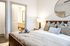 Stylish bedroom featuring a bed with layered pillows, soft lighting, and a view into a modern bathroom.