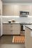 Contemporary kitchen with light wood cabinets, stainless steel appliances, and an orange striped rug.