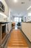 View from a modern kitchen with light wood cabinets and orange runner rug, leading into a bright living room with large windows.