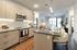 Modern kitchen with light wood cabinets, dark countertops, and barstool seating, opening into a bright living space.