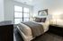Bedroom with large window, black nightstands, neutral bedding, and a wooden mirror above the bed.