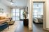 Modern apartment interior featuring a cozy living room with leather couch, sleek furnishings, and a view into a sunlit bedroom with large windows.