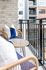 Outdoor balcony with two wicker chairs, navy and white cushions, and a round glass-top table overlooking a modern apartment complex.