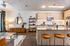 Modern open-concept kitchen with wood cabinetry, island seating, and adjacent living area with a sofa, glass coffee table, and decorative shelving.