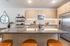 Contemporary kitchen with a large island featuring a built-in sink and seating, light wood cabinetry, stainless steel appliances, and open shelving.