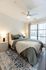 A bright and cozy bedroom with a tufted headboard, layered bedding in soft green and beige tones, modern nightstands, and large windows with natural light.