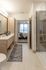 Modern bathroom with a glass shower, light wood vanity, and decorative runner, looking through an open door into a bright bedroom.