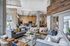 Modern apartment clubhouse lounge with multiple seating areas, stylish chandeliers, a television, and wood-accented walls.