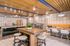 Modern community kitchen and dining area featuring wood accents, stainless steel appliances, a large island, communal tables with bench seating, and contemporary lighting.
