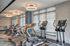 Modern fitness center with treadmills, ellipticals, and spin bikes arranged in a well-lit space with large windows and contemporary lighting fixtures.