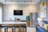Contemporary community kitchen featuring a marble island with barstools, stainless steel appliances, a mounted TV, modern backsplash, and cozy seating with accent pillows.