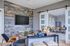 Modern community lounge with a wood accent wall, mounted TV, cozy seating, decorative accents, and sliding barn doors opening to a dining and kitchen space.