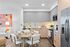 Modern apartment kitchen with sleek grey and wood cabinetry, stainless steel appliances, a round dining table set for four, and bright, colorful wall art in the adjoining living area.