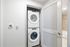 Compact laundry closet with a stacked Whirlpool washer and dryer unit, located next to a bathroom with light wood tile.