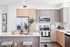 Bright and modern apartment kitchen with light wood cabinetry, stainless steel appliances, a central island with decorative plants and seating, and framed artwork on the wall.