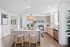Bright, modern kitchen with light wood cabinetry, a central island with two stools, stainless steel appliances, decorative plants, and wall art in a spacious, open layout.