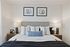 Modern bedroom with a tufted headboard, layered pillows in neutral tones, two matching bedside tables with lamps, and minimalist abstract art framed above the bed.