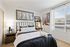 Cozy bedroom with a black metal headboard, neutral bedding, a nightstand with a lamp, and a ladder-style desk with decor, lit by natural light from a large window.