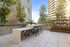 Outdoor grilling station with modern bar seating, geometric tile detail, and a vertical herb garden, surrounded by city buildings and trees.