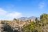 Scenic view of a mountain range under a clear blue sky, with trees and buildings in the foreground.