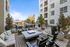 Outdoor courtyard lounge with firepit, cushioned seating, grill station, and dining area surrounded by modern apartment buildings and landscaping.