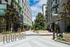 Open-air walkway between modern apartment buildings, featuring bike racks, potted plants, and landscaped greenery with trees and built-in planters.