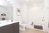 Bright bathroom with white walls and tile, a bathtub with a shower, sleek vanity with a dark cabinet, large mirror, and minimalist decor.