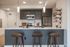 Contemporary kitchen with dark wood cabinets, stainless steel appliances, a large white island, and three modern bar stools under pendant lighting.
