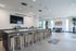 Spacious community kitchen with a large island, modern bar stools, stainless steel appliances, mounted TV, and a seating area with armchairs by the windows.
