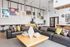 Contemporary lounge with modern sofas, a large wooden coffee table, and a gallery-style wall filled with framed art pieces under high ceilings.