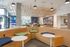 Stylish apartment lobby with curved wooden seating, round tables, modern light fixtures, and large windows bringing in natural light.