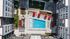 Aerial view of a rooftop pool surrounded by lounge chairs, red umbrellas, and modern apartment buildings in an urban setting.