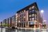 Contemporary apartment building with large windows and retail space at the ground level, illuminated during dusk.