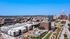 Aerial view of a city neighborhood featuring modern apartment buildings, a park with green space, and a variety of rooftops under a clear blue sky.