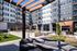 Modern outdoor lounge area with cushioned seating and a wooden pergola, surrounded by landscaped greenery and apartment buildings.