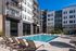 Resort-style courtyard pool surrounded by lounge chairs and modern apartment buildings under a clear blue sky.