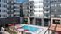 Courtyard pool area with red umbrellas, lounge chairs, and a wooden pergola surrounded by modern apartment buildings.