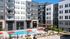 Courtyard pool area surrounded by lounge chairs, red umbrellas, greenery, and a modern mid-rise apartment building.