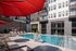 Modern courtyard pool with red umbrellas, lounge chairs, and a lift-accessible entry.