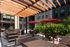 Covered outdoor seating area with cushioned chairs, red umbrellas, and greenery.