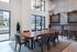 Modern entertainment kitchen and dining area with a long wooden table, high ceilings, bar seating, and large windows.