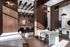 Contemporary lobby seating area with a long table, barstools, lounge chairs, and warm wood accents under decorative lighting.