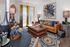 Colorful and modern living room featuring a leather sofa, abstract art, large windows with curtains, and a sliding glass door leading to a balcony.