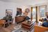 Stylish apartment living room with a modern wood coffee table, leather sofa, decorative accents, and large windows with curtains letting in natural light.